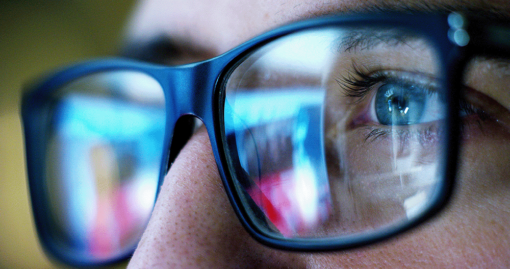Close up of computer screen reflecting into office worker's glasses.