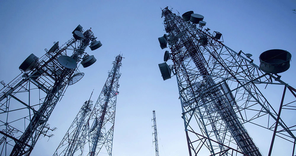 Close up of telecommunication masts showing TV antennas in front of blue sky.