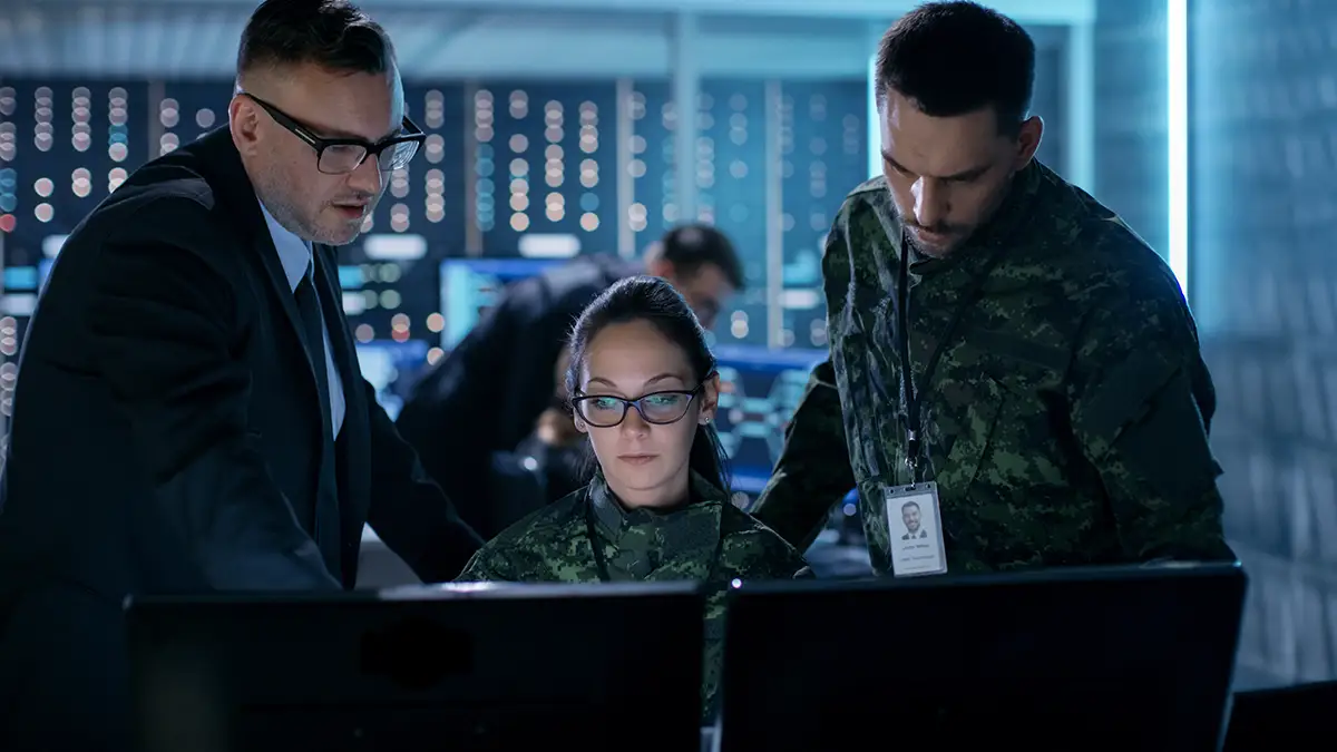 Two male government surveillance team members looking at female agents screen in network control center.