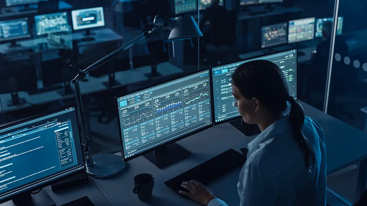 Female cyber security professional working at office desk, looking at dashboard showing network security posture.